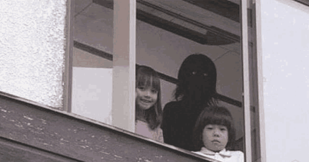 a group of children are looking out of a window with a silhouette of a person behind them .