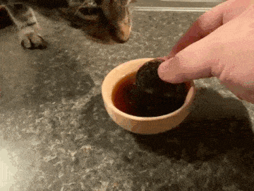 a person is dipping a cookie into a small bowl of sauce .