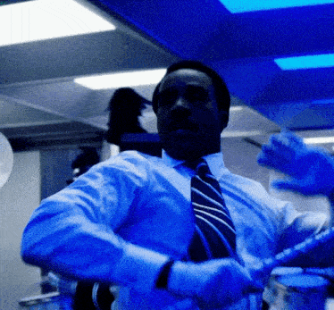 a man in a blue shirt and tie is dancing in a room