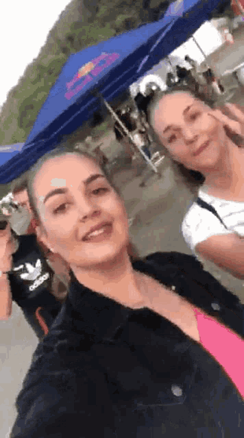 two women are posing for a selfie in front of a blue red bull tent