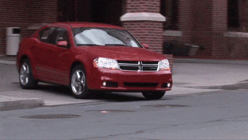 a red dodge car is driving down a street