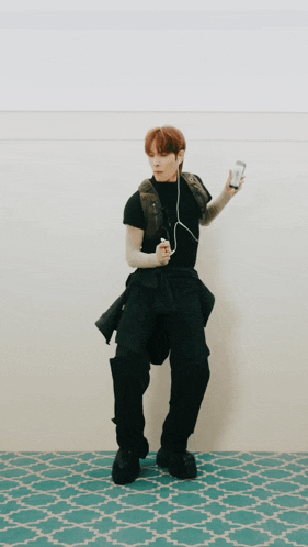 a man in a black shirt and black pants is standing in front of a wall holding a can of soda