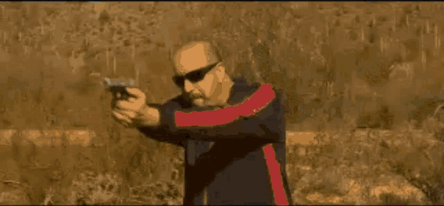a man is holding a gun and jumping over a blue barrel in the desert