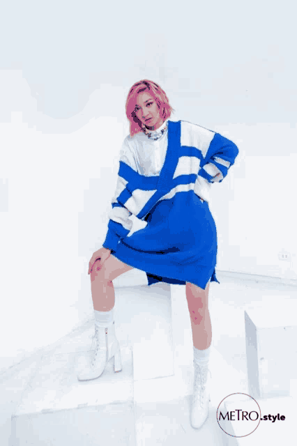 a woman with pink hair is wearing a blue and white sweater and white boots