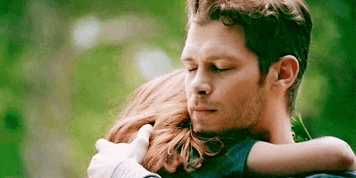 a man and a woman are hugging each other in a forest .