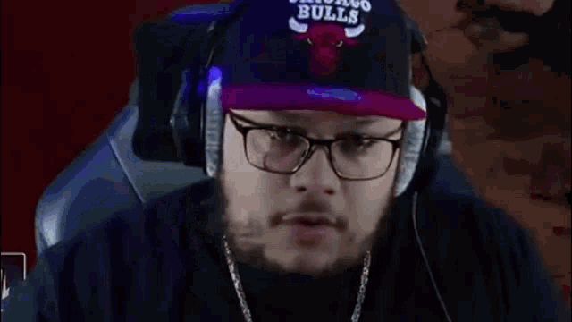 a man wearing a chicago bulls hat and glasses is sitting in a chair .