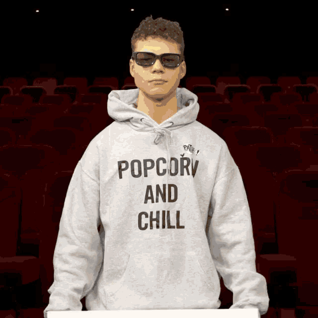 a man wearing a popcorn and chill hoodie stands in an auditorium