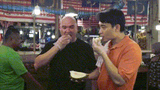 a man in an orange shirt is eating a slice of food