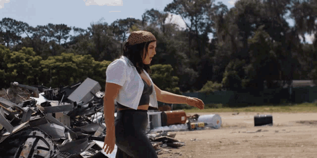 a woman in a white shirt and black pants is walking through a pile of trash