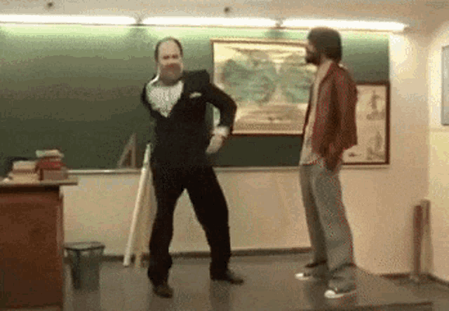 two men are dancing in front of a green board