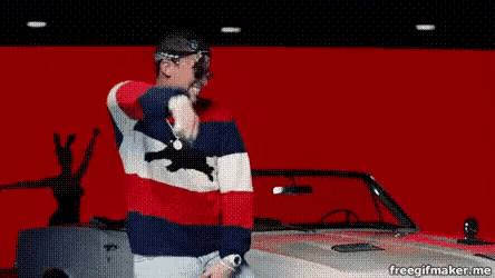 a man in a striped sweater is standing in front of a red car .