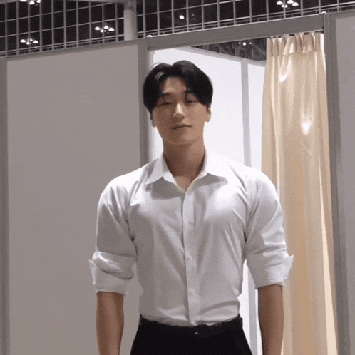 a man in a white shirt and black pants stands in front of a white wall