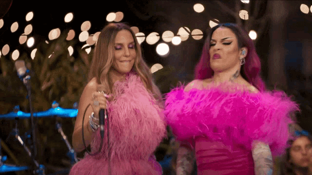 a woman in a pink feathered dress singing into a microphone