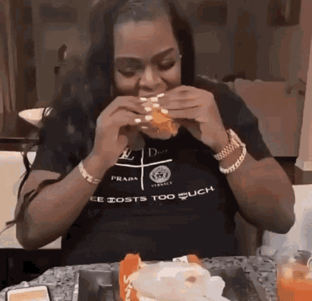 a woman is eating a hamburger while wearing a prada shirt .