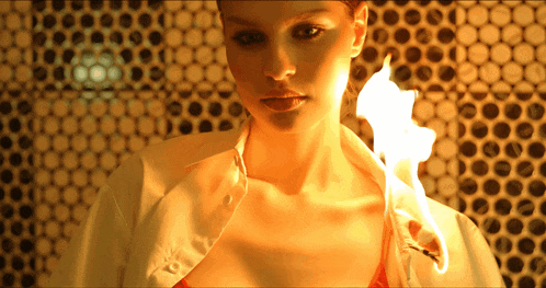 a woman in a white shirt is holding a piece of paper on fire