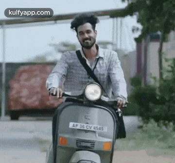a man is riding a scooter down a road and smiling .