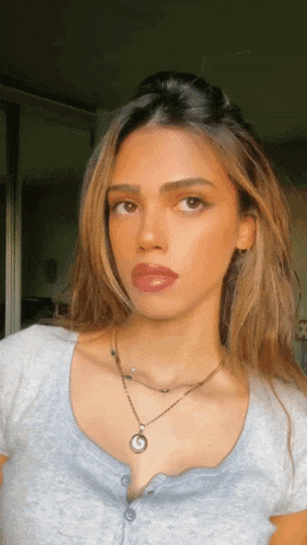 a woman wearing a grey shirt and a necklace with a round pendant