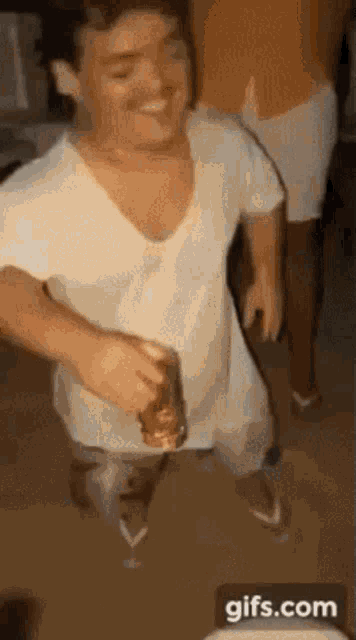 a man in a white shirt and flip flops is holding a bottle of beer .