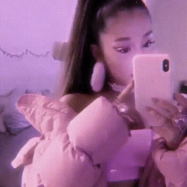 ariana grande is taking a selfie with her cell phone while holding a pink teddy bear .
