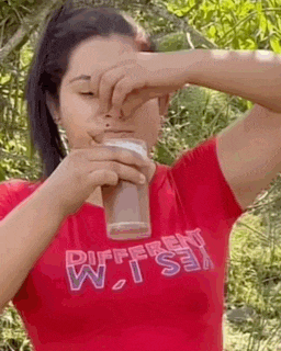 a woman in a red shirt is holding a glass of milk in front of her face .