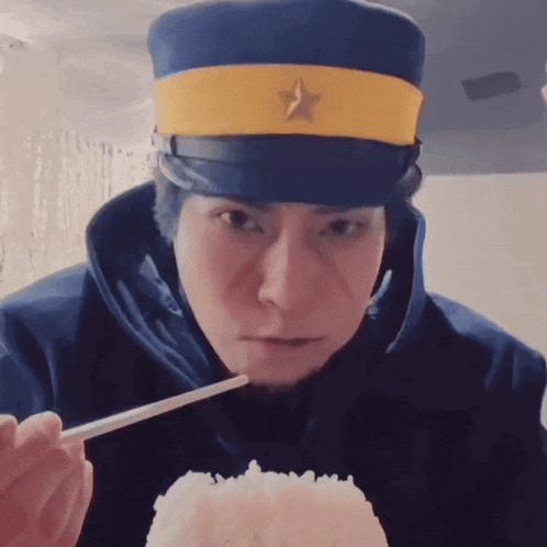 a man wearing a blue hat with a yellow star on it eating rice with chopsticks