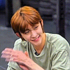 a young man with red hair is smiling while sitting at a table with his hands folded .