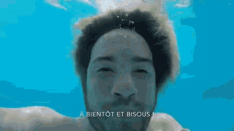 a man with a beard is swimming underwater with the words a bientot et bisous above him