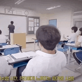 a group of people are sitting at desks in a classroom with foreign writing on the bottom of the screen
