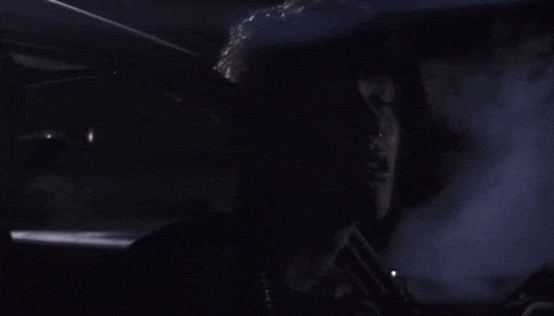 a man is sitting in a dark room with smoke coming out of the window
