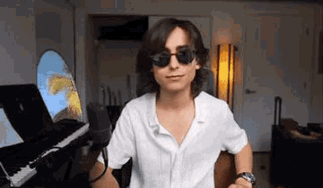 a young man wearing sunglasses is standing in front of a piano .