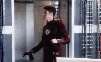 a man in a flash costume is standing in a doorway holding a bottle .