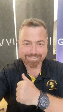 a man with a beard is giving a thumbs up and wearing a watch .