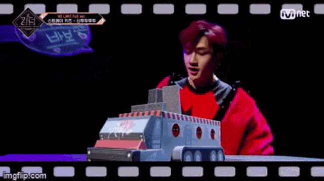 a man in a red sweater is standing next to a toy truck with the word jyp on it