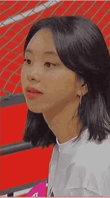 a close up of a woman 's face with a red background . she is wearing a white shirt and earrings .