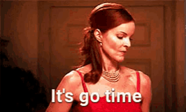 a woman in a red dress is standing in front of a door and saying it 's go time .