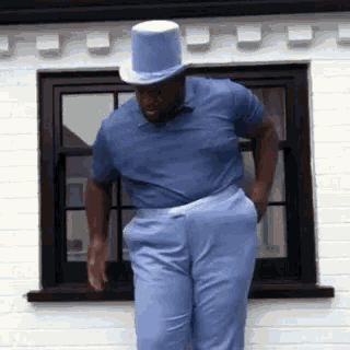 a man wearing a top hat and a blue shirt is standing in front of a window