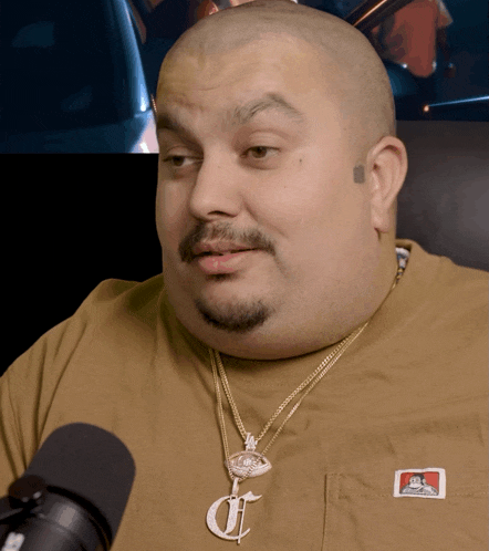 a man wearing a ben davis shirt and a necklace with the letter c on it