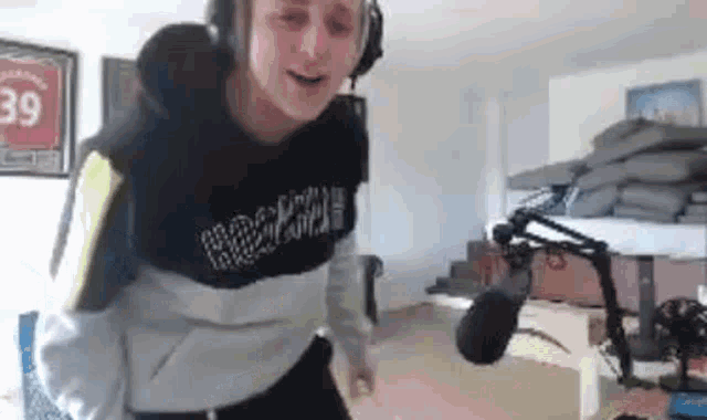 a man wearing headphones and a sweatshirt is standing in front of a microphone in a room .