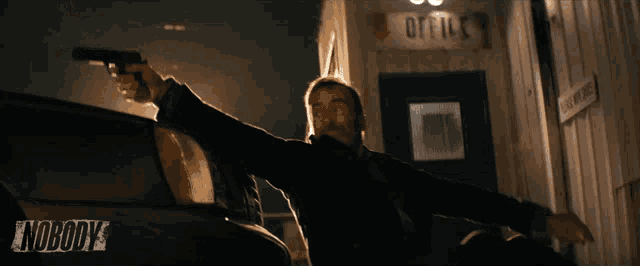 a man holding a gun in front of a building that says office on it