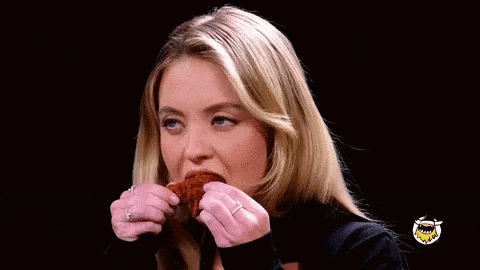 a woman is eating a chicken wing with her eyes closed .