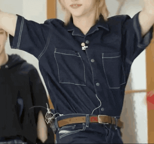 a woman wearing a blue shirt and a brown belt is dancing with her arms outstretched