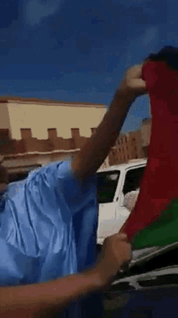 a man in a blue shirt is holding a red and green flag in front of a white car