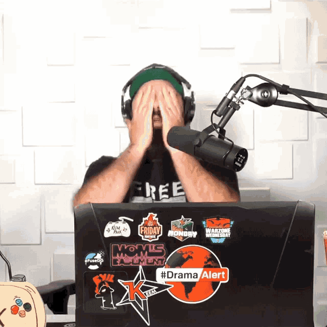 a man wearing headphones covering his face in front of a laptop that says #dramaalert on it