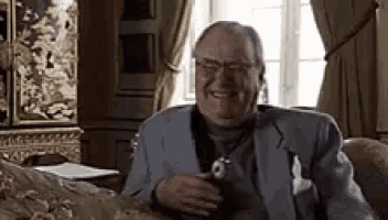 a man in a suit and tie is sitting on a couch holding a watch and smiling .