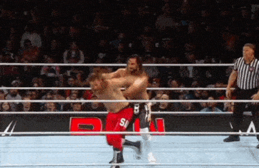 two wrestlers are wrestling in a ring with a referee watching