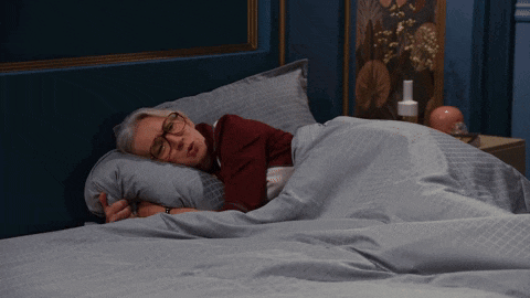 a woman wearing glasses is sleeping on a bed with a blue blanket