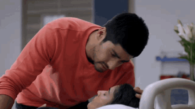 a man in a red shirt is putting his hand on a woman 's head in a hospital bed