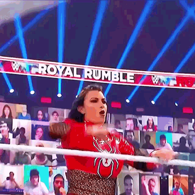 a woman is standing in a wrestling ring with a sign that says royal rumble in the background .