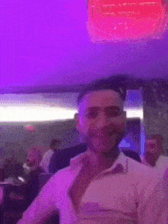 a man in a white shirt is dancing in a club with purple lights