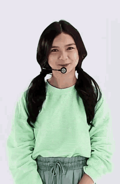 a young woman wearing a green sweater and green pants is wearing a microphone around her neck .